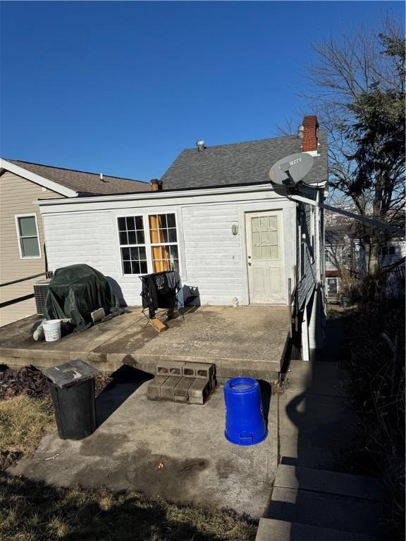 rear view of house with a patio, roof with shingles, and a chimney