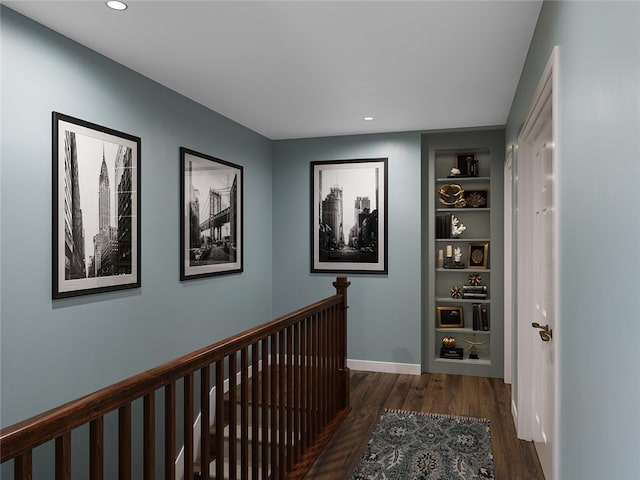 hallway with built in shelves, wood finished floors, baseboards, recessed lighting, and an upstairs landing