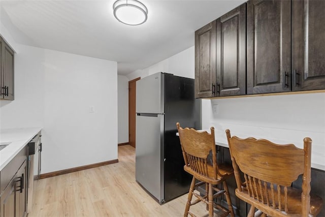 kitchen with baseboards, light wood finished floors, dark brown cabinets, and freestanding refrigerator