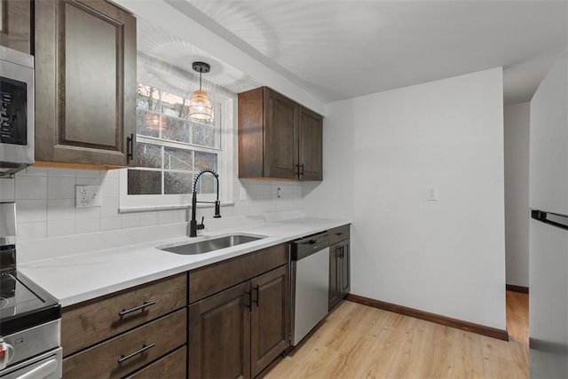 kitchen featuring tasteful backsplash, light countertops, appliances with stainless steel finishes, light wood-style floors, and a sink