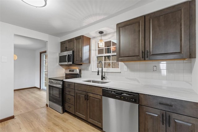 kitchen featuring light wood-style flooring, a sink, stainless steel appliances, dark brown cabinetry, and backsplash