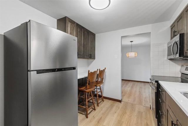 kitchen featuring dark brown cabinets, backsplash, baseboards, light wood-style flooring, and appliances with stainless steel finishes