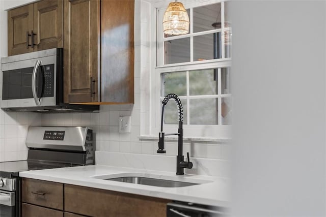 kitchen featuring a healthy amount of sunlight, a sink, stainless steel appliances, light countertops, and backsplash