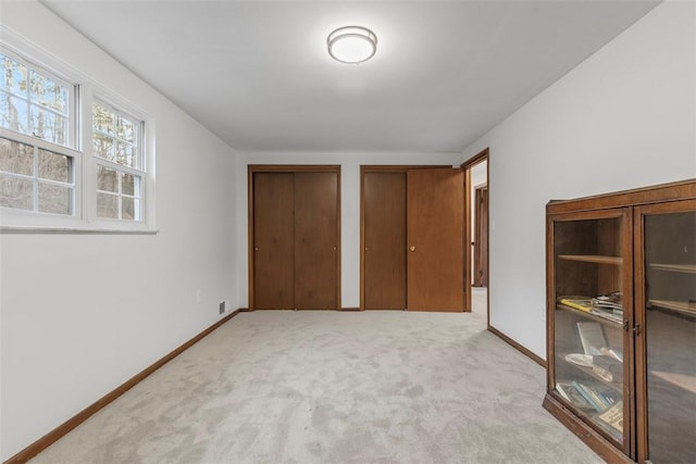 unfurnished bedroom with baseboards, carpet floors, two closets, and visible vents