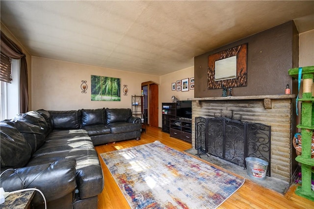 living area with arched walkways, a brick fireplace, and wood finished floors