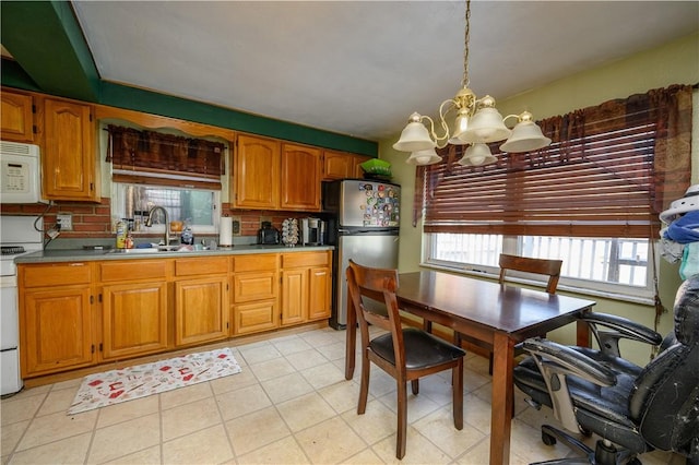 kitchen with a sink, white appliances, an inviting chandelier, and brown cabinetry