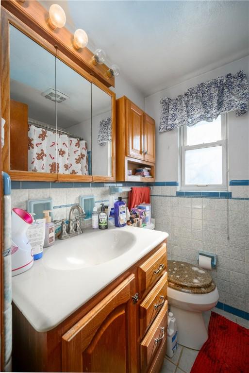 bathroom with tile patterned flooring, visible vents, toilet, vanity, and tile walls