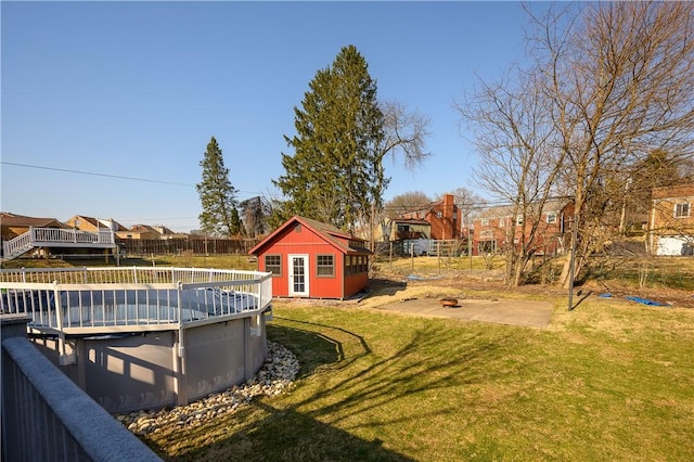 view of yard featuring an outbuilding, an outdoor fire pit, fence, a residential view, and an outdoor pool