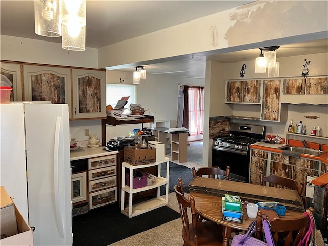 kitchen with stainless steel range with gas stovetop, carpet flooring, freestanding refrigerator, and a sink