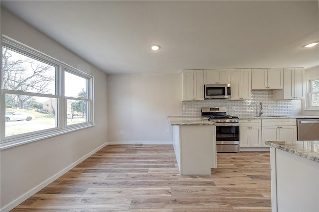 kitchen featuring a wealth of natural light, backsplash, stainless steel appliances, and light wood-style flooring