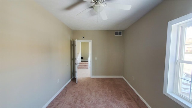 carpeted spare room featuring plenty of natural light, baseboards, visible vents, and ceiling fan