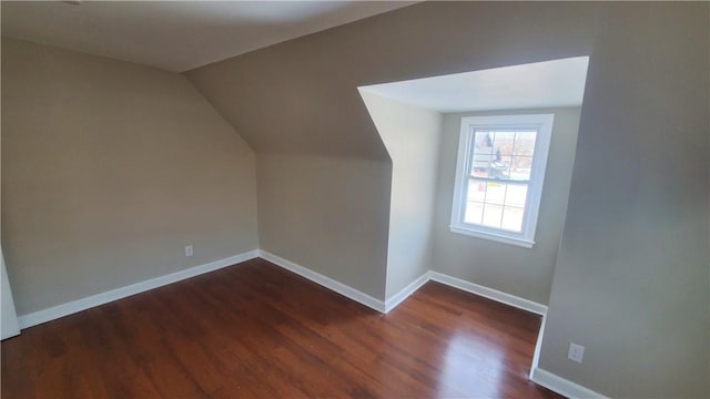 additional living space featuring dark wood finished floors, baseboards, and vaulted ceiling