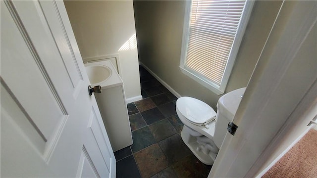 bathroom featuring vanity, toilet, baseboards, and stone tile flooring