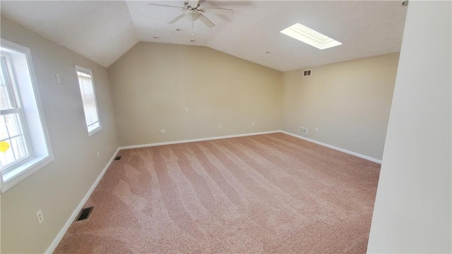 spare room with vaulted ceiling with skylight, a ceiling fan, visible vents, and light carpet