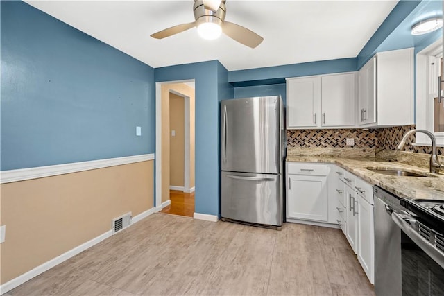 kitchen with visible vents, light stone countertops, stainless steel appliances, white cabinetry, and a sink