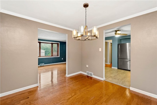 empty room featuring crown molding, wood finished floors, visible vents, and baseboards