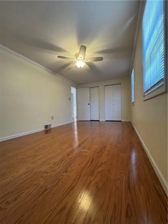 unfurnished bedroom with visible vents, multiple closets, ornamental molding, wood finished floors, and baseboards