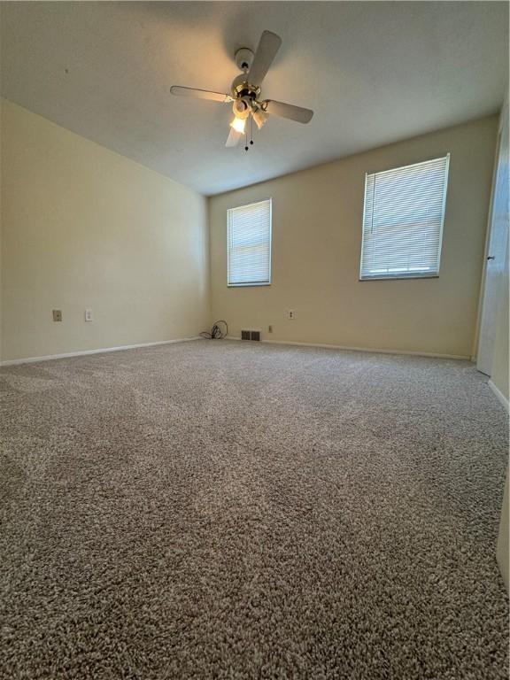 carpeted empty room with a ceiling fan, visible vents, and baseboards