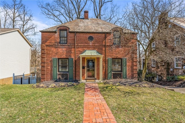 view of front of property with brick siding, a chimney, a front lawn, and fence