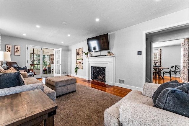 living area with visible vents, a fireplace with flush hearth, wood finished floors, recessed lighting, and baseboards