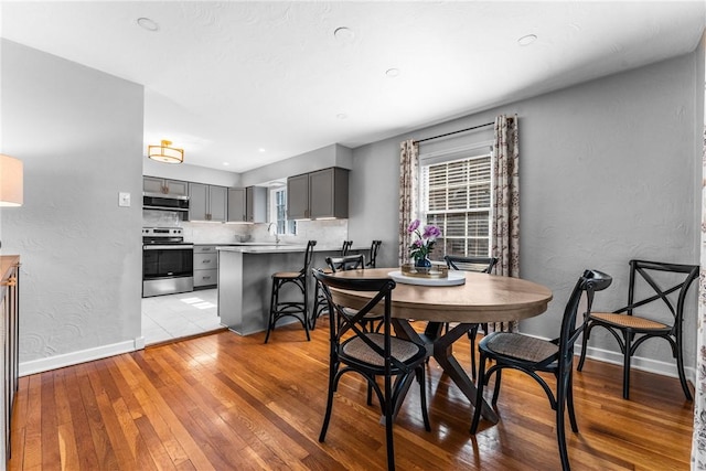 dining space featuring a textured wall, baseboards, and light wood finished floors