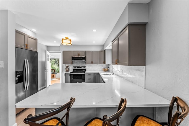 kitchen with gray cabinets, a sink, light stone counters, tasteful backsplash, and appliances with stainless steel finishes