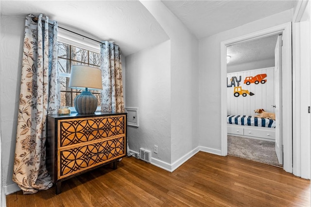 hallway featuring a textured ceiling, wood finished floors, visible vents, and baseboards