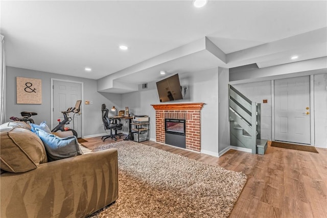 living area with stairway, a brick fireplace, light wood-type flooring, and baseboards