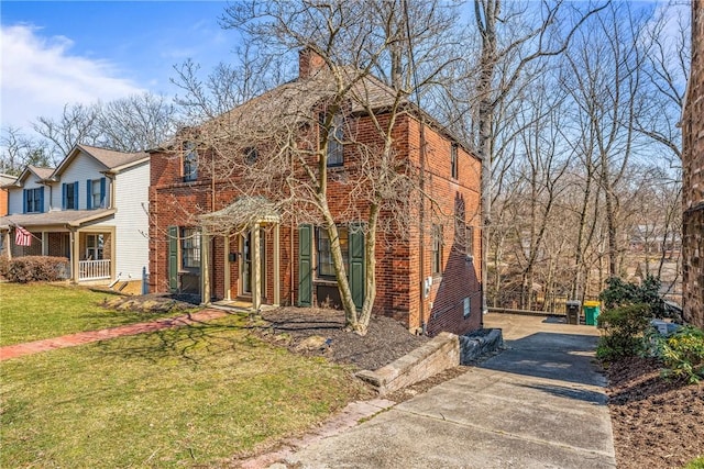 view of front of house with brick siding, driveway, a chimney, and a front lawn