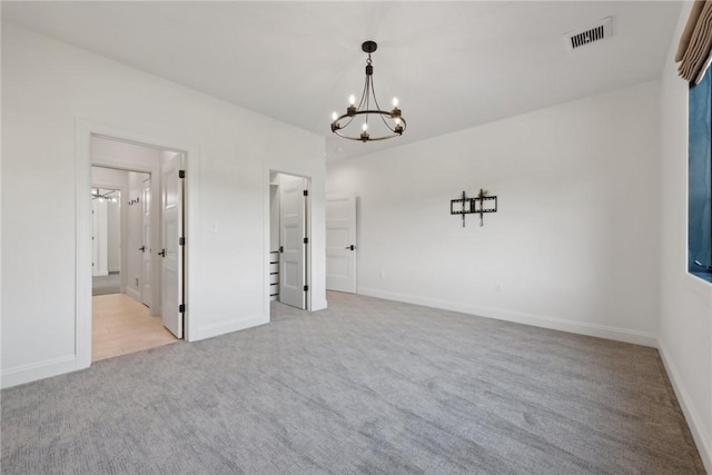 carpeted empty room with visible vents, baseboards, and a chandelier