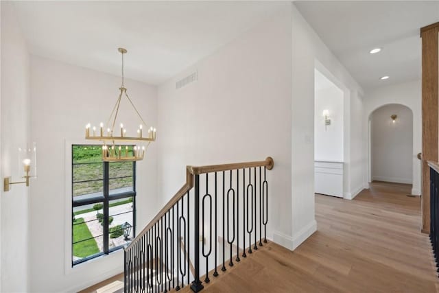 corridor featuring visible vents, an upstairs landing, light wood-style floors, an inviting chandelier, and arched walkways