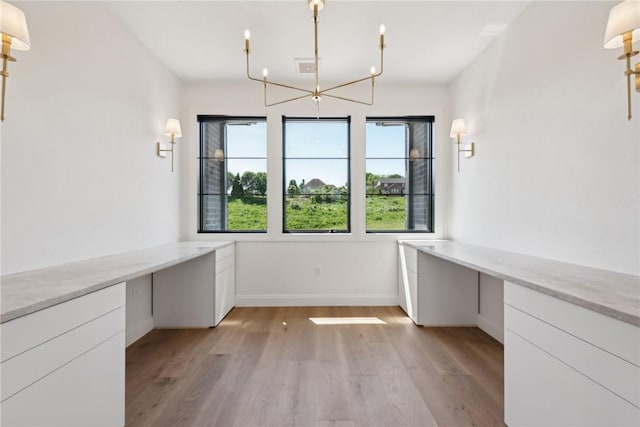 unfurnished dining area with a chandelier, baseboards, and light wood-style flooring