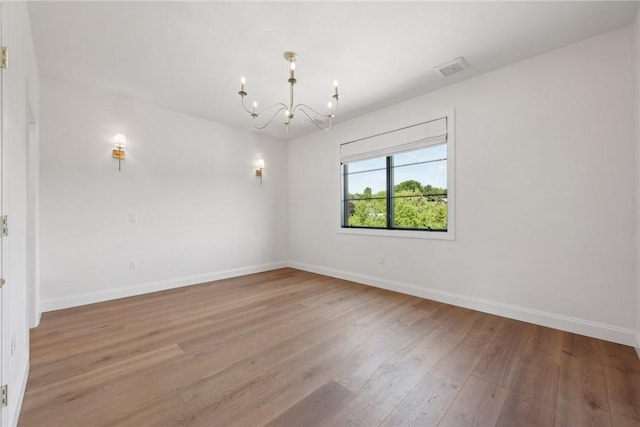 empty room featuring a chandelier, baseboards, and wood finished floors