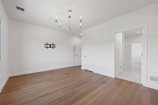 unfurnished room featuring baseboards, wood finished floors, visible vents, and a chandelier