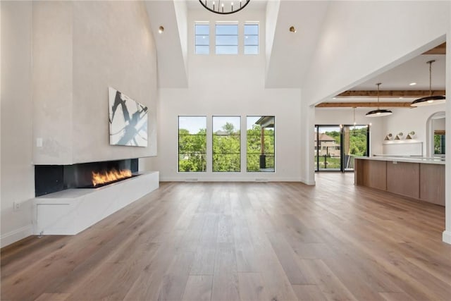 unfurnished living room featuring a notable chandelier, light wood-type flooring, a large fireplace, and baseboards