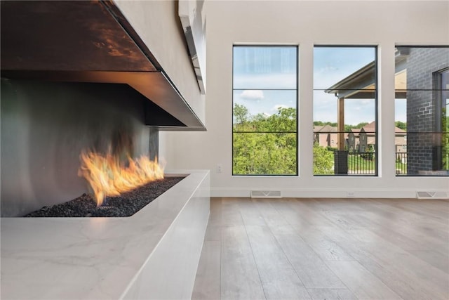 interior space featuring visible vents, baseboards, a lit fireplace, and wood finished floors