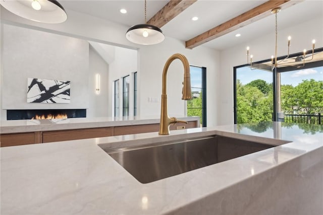 kitchen with a sink, beamed ceiling, light stone counters, and hanging light fixtures