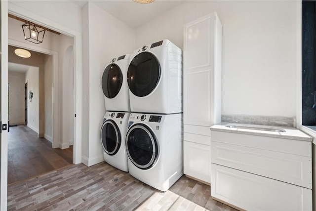 laundry room with cabinet space, stacked washing maching and dryer, and light wood-type flooring