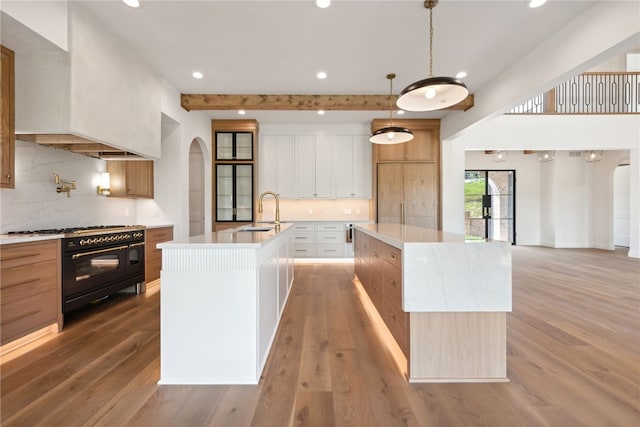 kitchen with a kitchen island with sink, a sink, arched walkways, range with two ovens, and custom exhaust hood