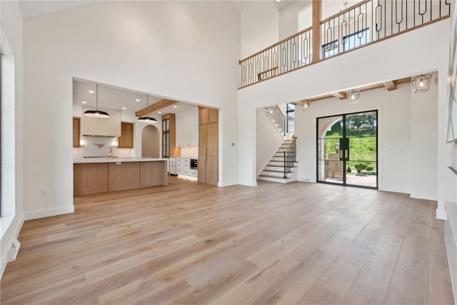 unfurnished living room featuring baseboards, stairway, recessed lighting, light wood-style floors, and a towering ceiling