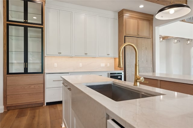 kitchen featuring a sink, light stone counters, wood finished floors, white cabinets, and decorative backsplash