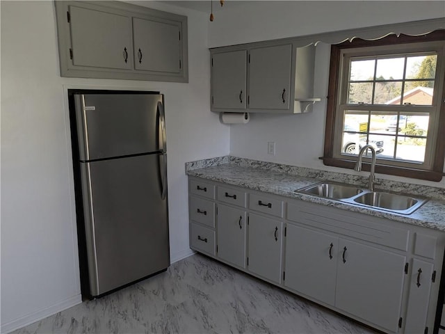 kitchen featuring baseboards, light countertops, freestanding refrigerator, marble finish floor, and a sink