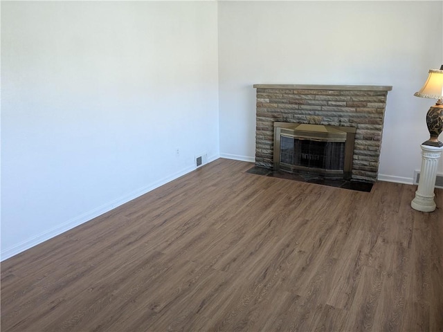 unfurnished living room with a stone fireplace, dark wood-style floors, visible vents, and baseboards