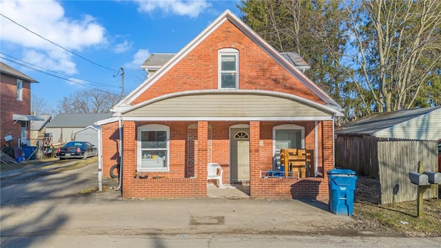 view of front of house with a porch, brick siding, and fence