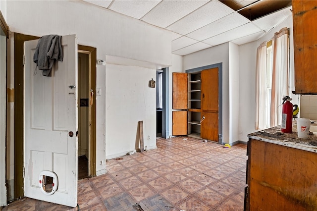 interior space with a drop ceiling, light floors, and baseboards