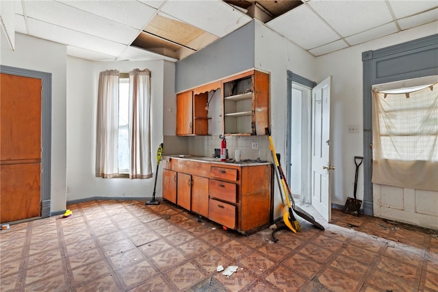 kitchen featuring tasteful backsplash, a drop ceiling, light floors, brown cabinetry, and open shelves