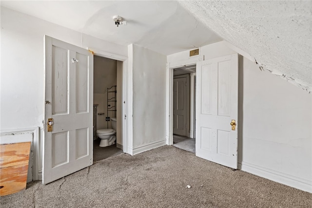 unfurnished bedroom featuring ensuite bath, carpet flooring, and visible vents