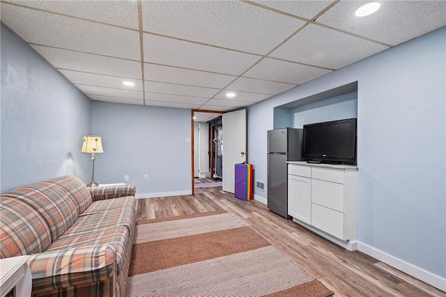 unfurnished living room with light wood-style flooring, a paneled ceiling, and baseboards