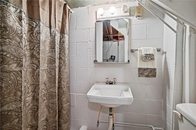 full bathroom featuring toilet, a shower with shower curtain, concrete block wall, and a sink