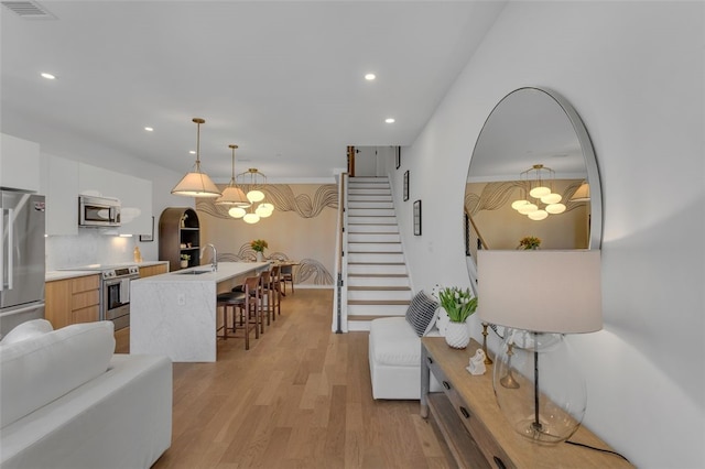 living room with stairway, an inviting chandelier, light wood-style flooring, and visible vents